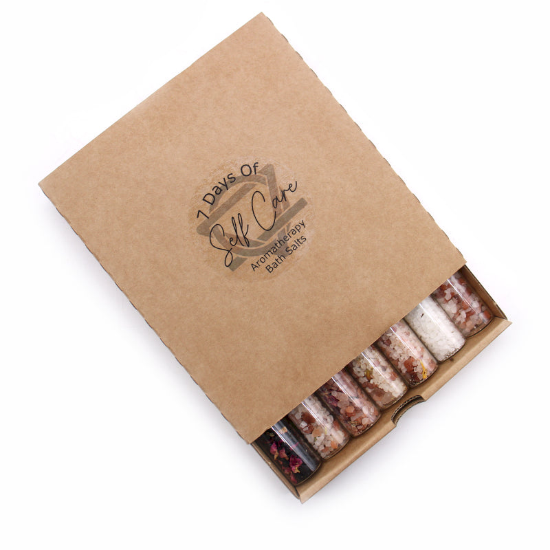 Kraft paper box containing 7 small bottles of bath salts with '7 Days of Self Care' branding.